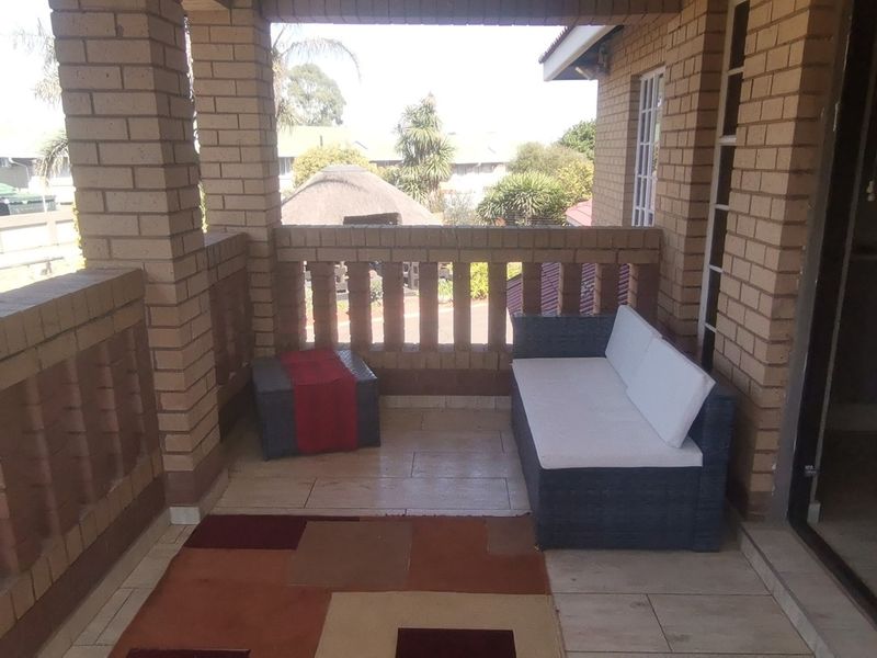 A covered balcony featuring brick pillars and balustrades with tiled flooring, providing an outdoor space accessible through a sliding glass door.