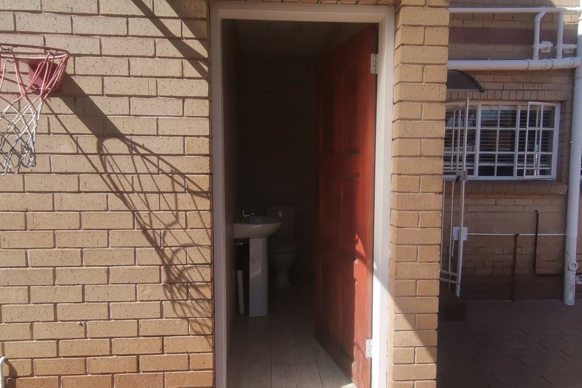Exterior view of a rear brick facade featuring an outdoor access door leading to a small bathroom with a pedestal basin and toilet.