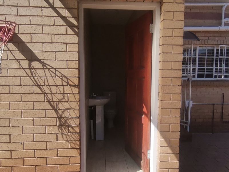 Exterior view of a rear brick facade featuring an outdoor access door leading to a small bathroom with a pedestal basin and toilet.