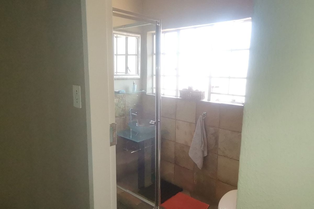 A functional bathroom featuring a glass shower enclosure, tiled wall finishes, and a pedestal basin with natural light from the window.