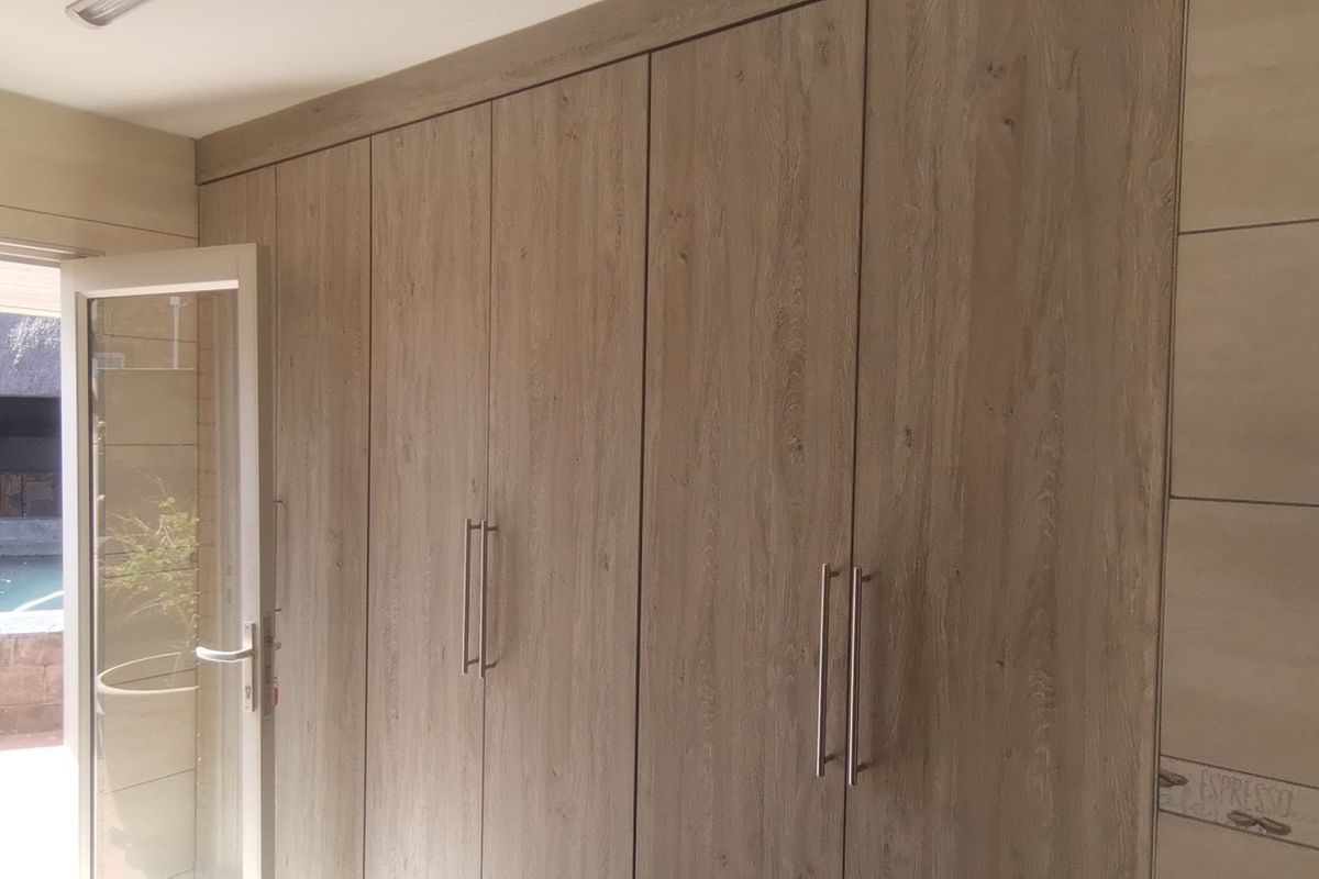 A bright bedroom featuring modern wood-finish built-in cupboards and direct access to an outdoor patio area.