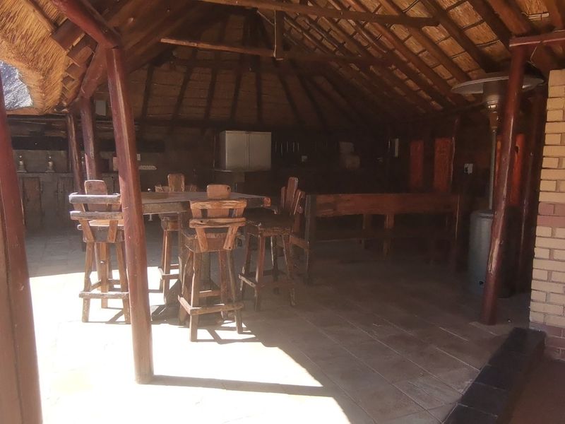 Covered outdoor patio area featuring a traditional thatched roof, timber support structure, tiled flooring, and a built-in braai facility.