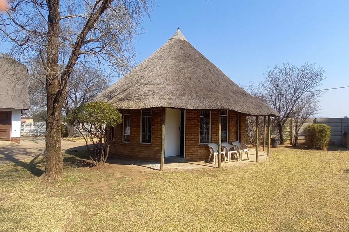 A detached circular dwelling featuring a traditional thatch roof, exposed brick exterior, and a covered veranda set within a spacious garden area.