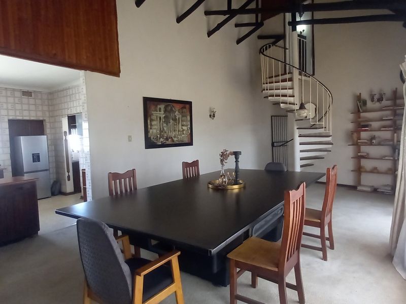 Spacious open-plan living and dining area featuring a distinctive spiral staircase, exposed timber beams, and an adjoining kitchen with dated finishes.