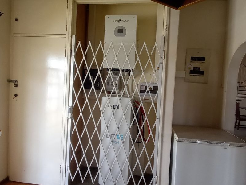 Utility area featuring a wall-mounted solar inverter and lithium battery storage system secured behind a metal gate.