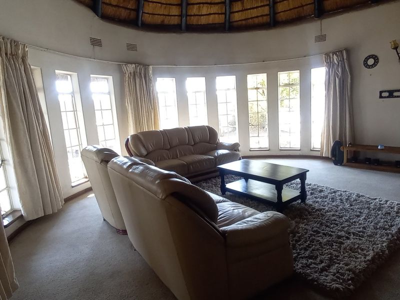 Spacious circular living room featuring a unique thatched roof, curved walls with multiple windows, and an exposed stone feature wall.