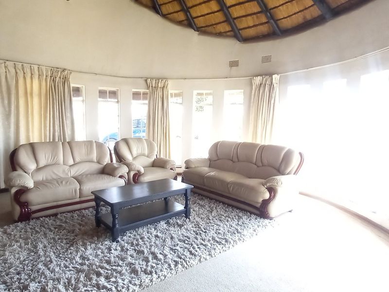 A spacious circular living room featuring a unique thatched roof, stone accent wall, and large windows that provide ample natural light.