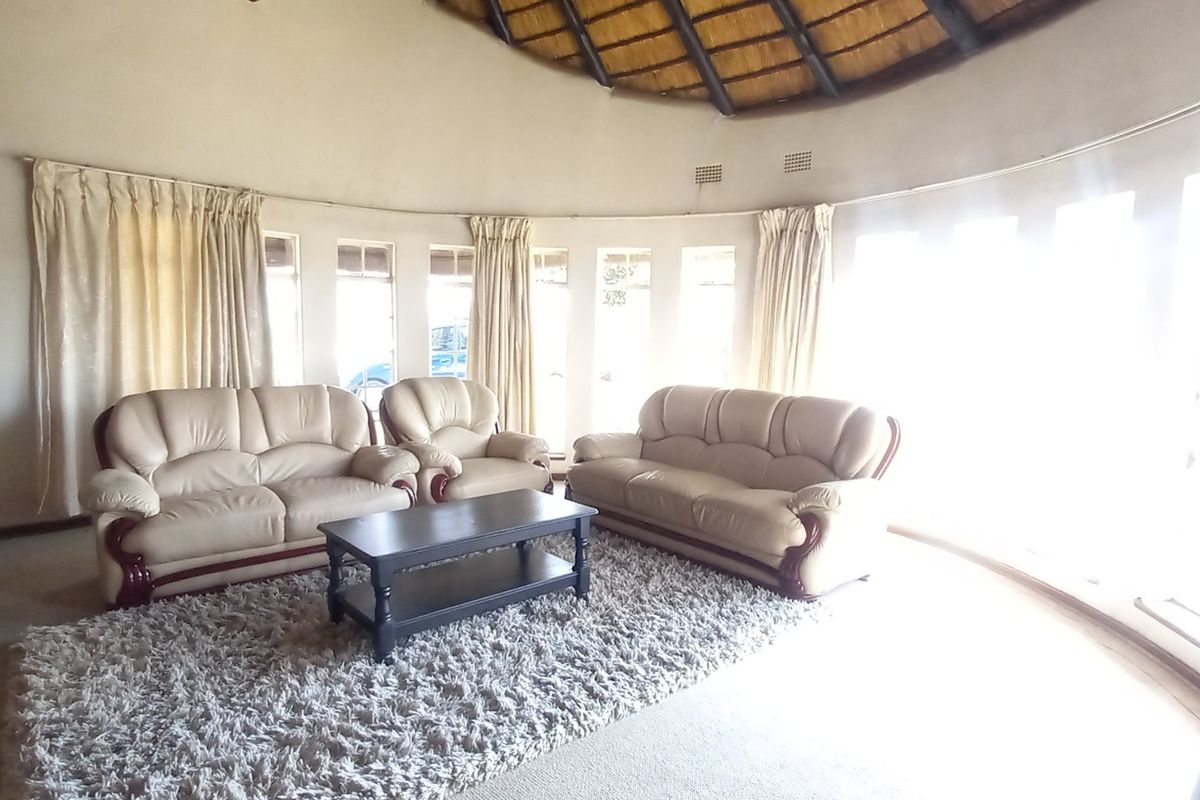 A spacious circular living room featuring a unique thatched roof, stone accent wall, and large windows that provide ample natural light.