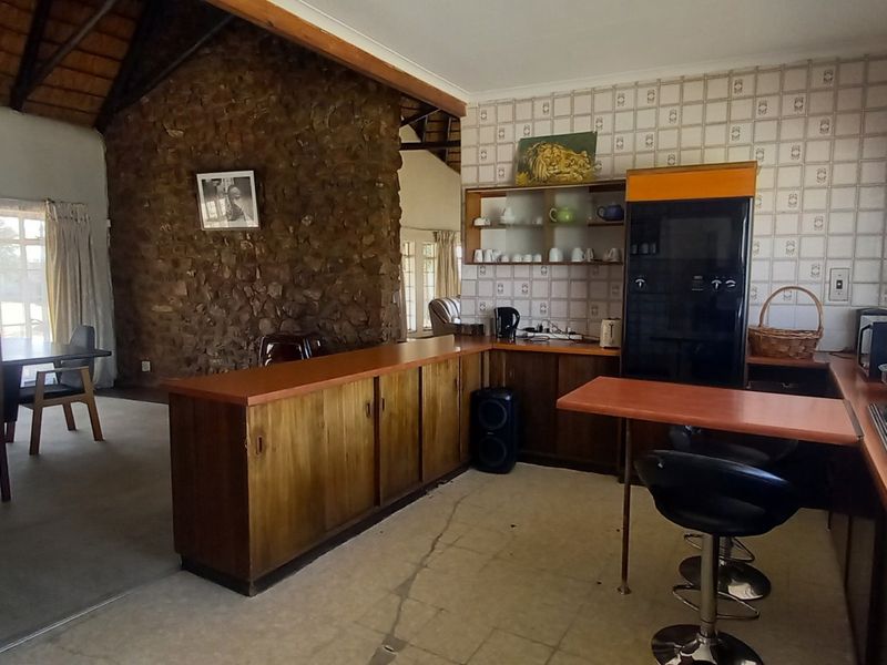 Open-plan kitchen and living area featuring a rustic stone feature wall, vaulted ceilings with exposed beams, and dated cabinetry with tiled splashbacks.