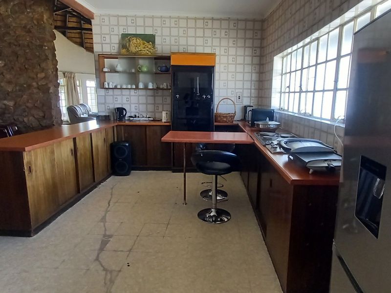 Spacious kitchen featuring dated wooden cabinetry, laminate countertops, a stone feature wall, and large windows, offering significant potential for a modern renovation.