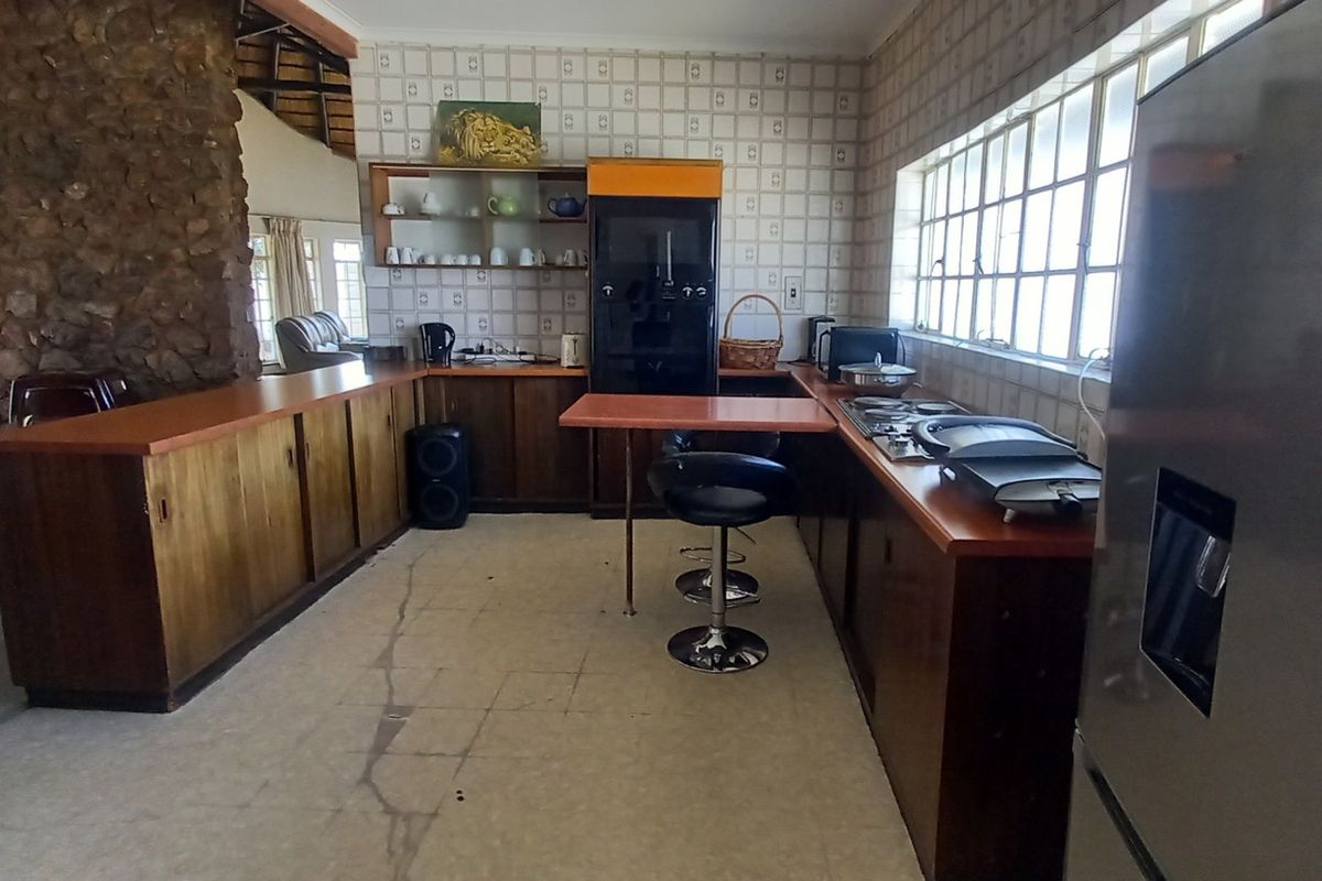 Spacious kitchen featuring dated wooden cabinetry, laminate countertops, a stone feature wall, and large windows, offering significant potential for a modern renovation.