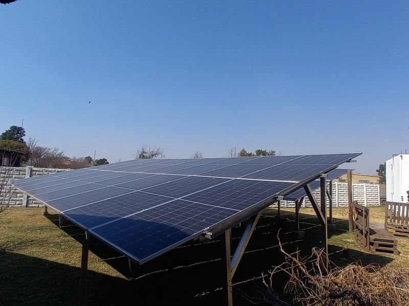 A ground-mounted solar panel array installed in the backyard, featuring a sturdy metal frame and surrounded by a precast concrete boundary wall.