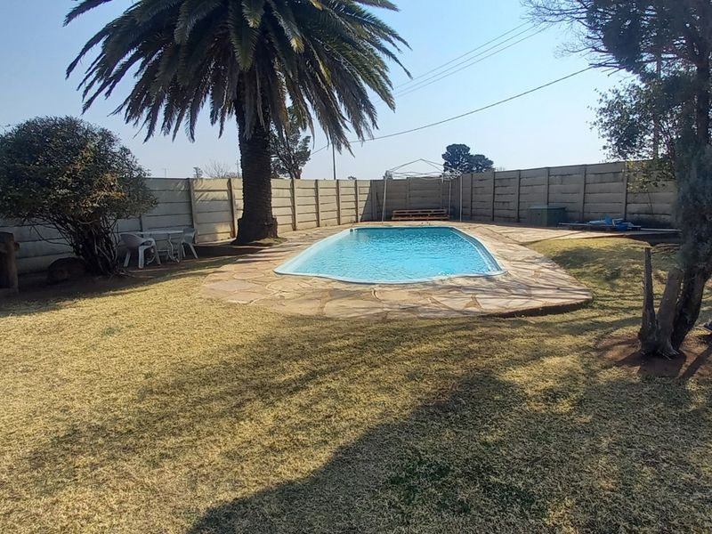 Outdoor pool area featuring a swimming pool, stone paving, and a built-in braai, enclosed by a precast concrete boundary wall.