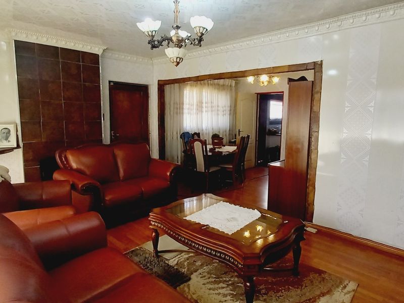 A traditional living room featuring hardwood flooring, a tiled fireplace, and decorative ceiling cornicing, offering a classic layout with access to the dining area.