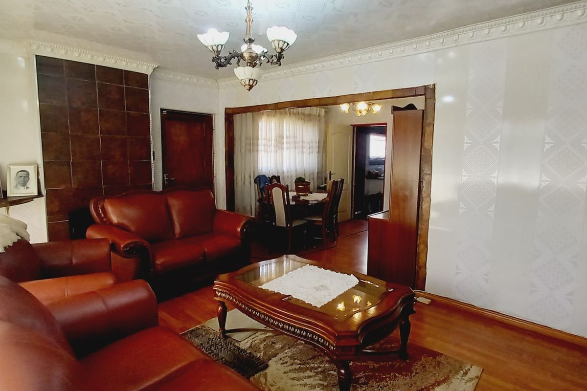 A traditional living room featuring hardwood flooring, decorative crown molding, and a tiled fireplace surround, with an open transition to the dining area.