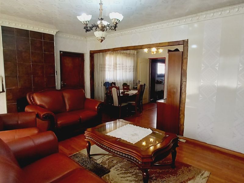 A traditional living room featuring hardwood flooring, decorative crown molding, and a tiled fireplace surround, with an open transition to the dining area.