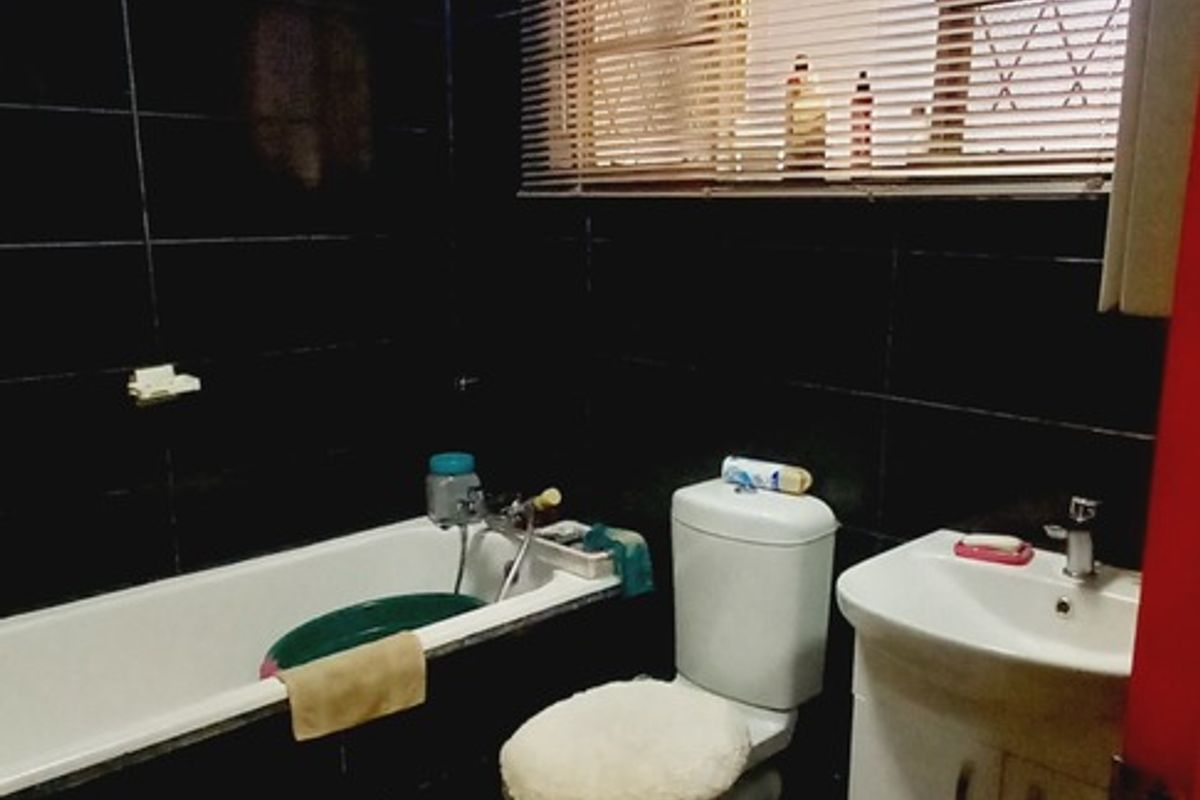 A compact bathroom featuring dark wall tiles, marble-effect floor tiles, a standard bathtub, a vanity basin, and a toilet.