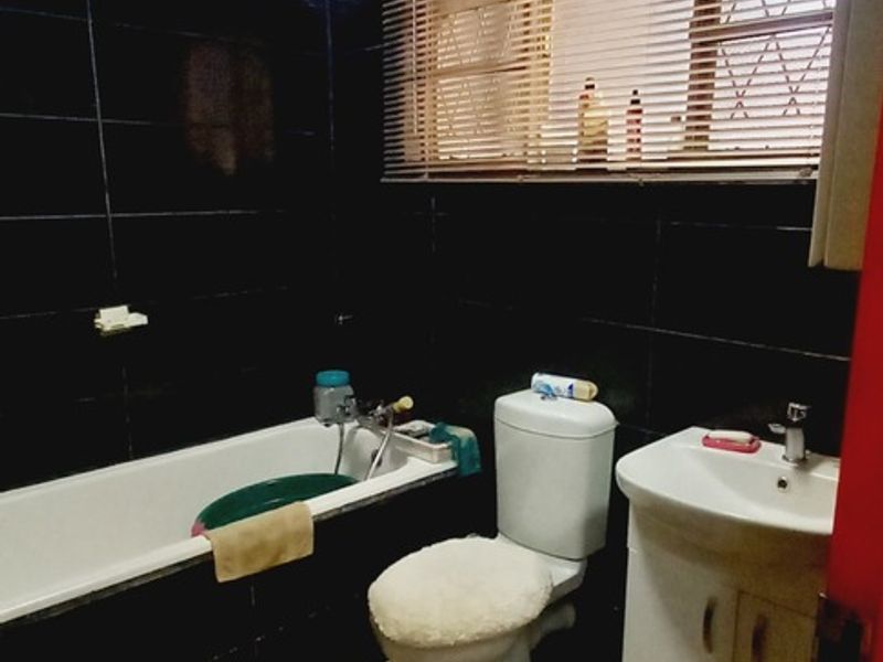 A compact bathroom featuring dark wall tiles, marble-effect floor tiles, a standard bathtub, a vanity basin, and a toilet.
