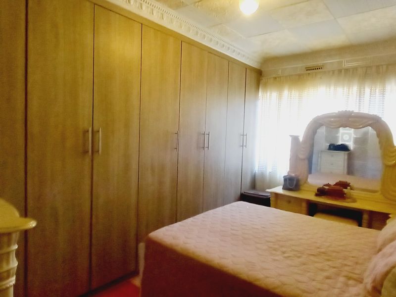 A bedroom featuring extensive built-in wooden cupboards and traditional ceiling tiles, offering ample storage space within a dated interior setting.