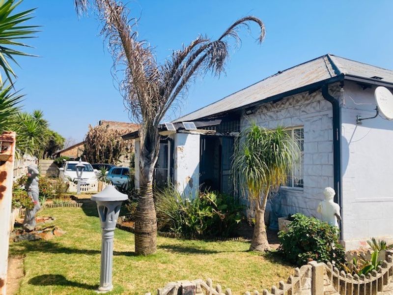 Front elevation of a single-story house featuring concrete block walls, a pitched roof, and a small front garden area with security fencing.
