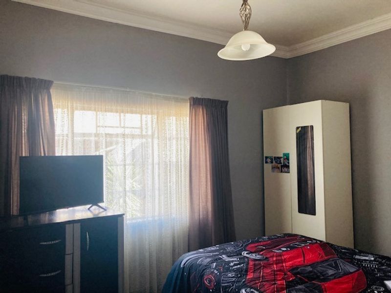 A functional bedroom featuring a built-in wardrobe, decorative ceiling cornice, and a central pendant light fixture.