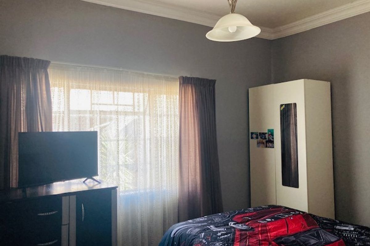 A functional bedroom featuring a built-in wardrobe, decorative ceiling cornice, and a central pendant light fixture.