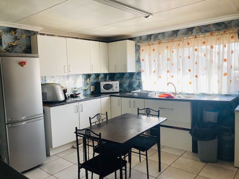 A functional kitchen featuring white built-in cabinetry, laminate countertops, a double basin sink, and tiled flooring, offering potential for modern updates.