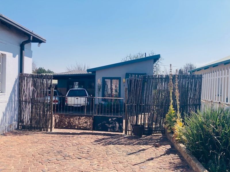 Front exterior view of the property featuring a cobblestone driveway, a metal gate, and a carport area.