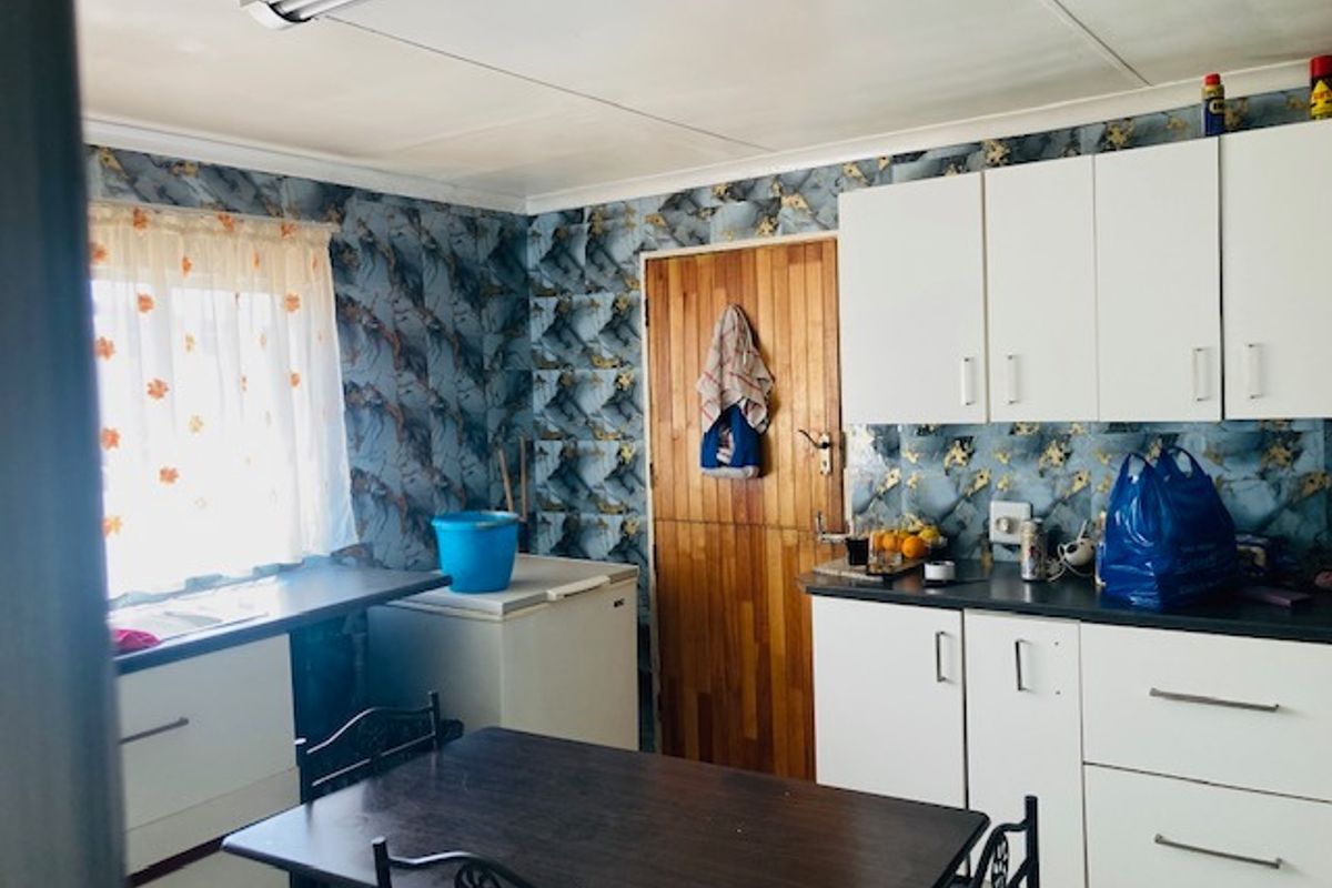 A functional kitchen space featuring white cabinetry, laminate countertops, and a timber door, currently requiring cosmetic updates to modernize the interior finishes.