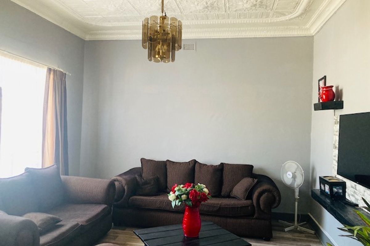 A living room featuring a classic ornate pressed metal ceiling with a decorative rose, complemented by modern laminate flooring.