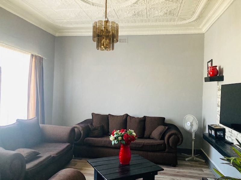 A living room featuring a classic ornate pressed metal ceiling with a decorative rose, complemented by modern laminate flooring.