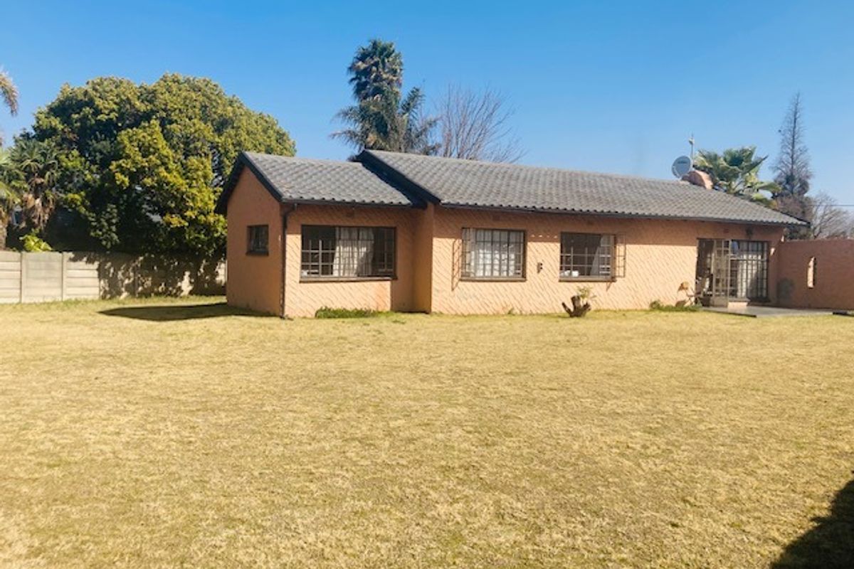 Rear view of a single-story brick house featuring a tiled roof, security bars on windows, and a large open lawn area.