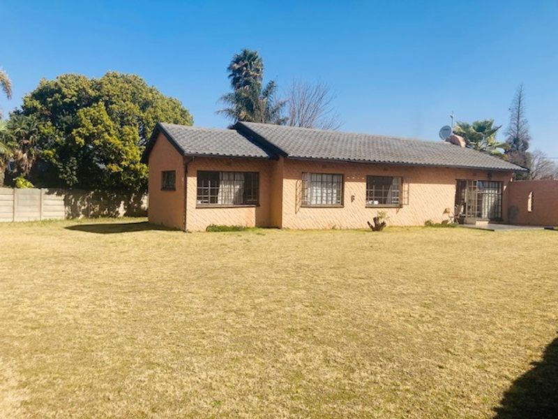 Rear view of a single-story brick house featuring a tiled roof, security bars on windows, and a large open lawn area.
