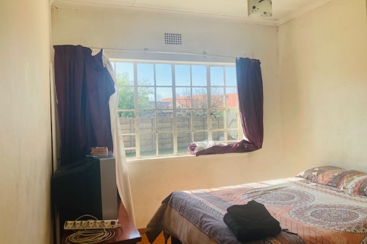 A bedroom featuring a steel-framed window with natural light, requiring cosmetic updates to the wall finishes.