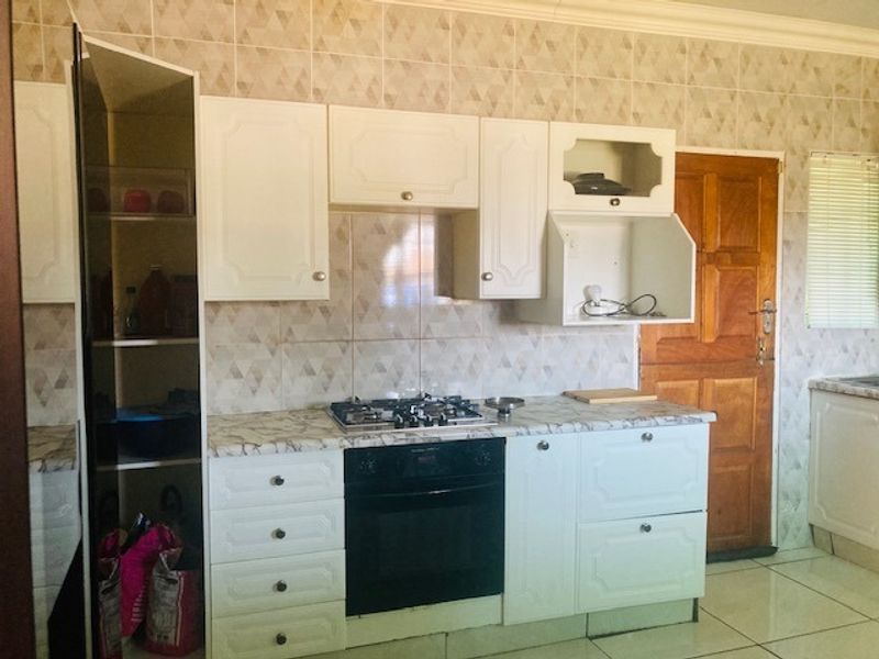 A functional kitchen featuring white cabinetry, a gas hob, built-in oven, tiled backsplash, and tiled flooring with direct access to an exterior door.