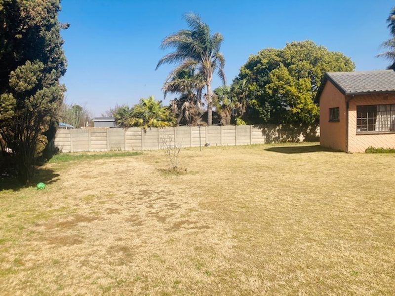 A spacious rear garden featuring a large lawn area, enclosed by a precast concrete boundary wall, with a view of the side of the house.