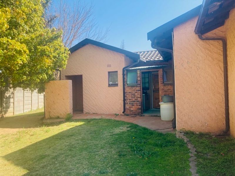Rear view of the house featuring textured stucco walls, exposed brick accents, a tiled roof, and a paved pathway leading to the entrance.