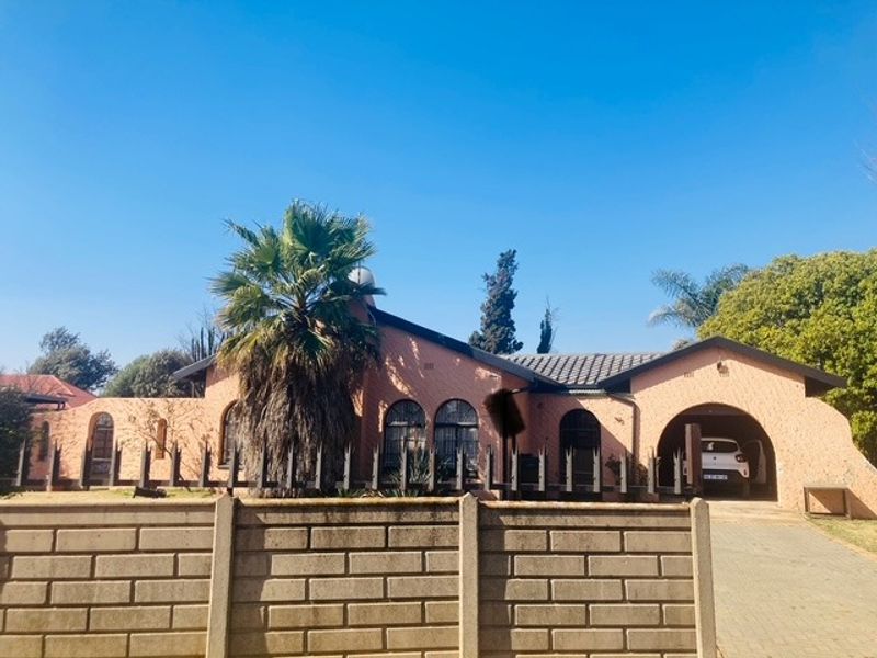 Front elevation of a single-story house featuring an arched entrance, a paved driveway, and a concrete boundary wall.