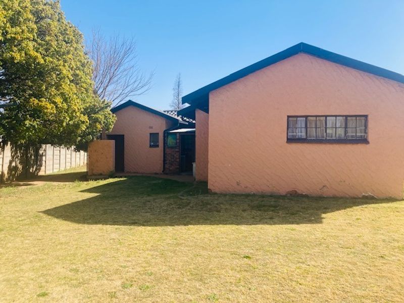 Rear view of the property showing the exterior stucco walls, steel-framed windows, and a surrounding precast concrete boundary wall with a grass lawn.