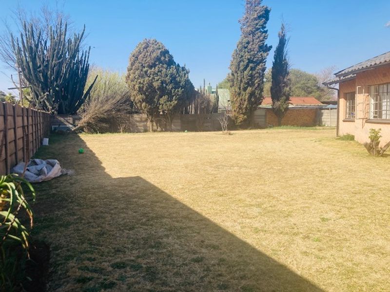 A spacious rear garden featuring a large lawn area, mature trees, and a precast concrete boundary wall.