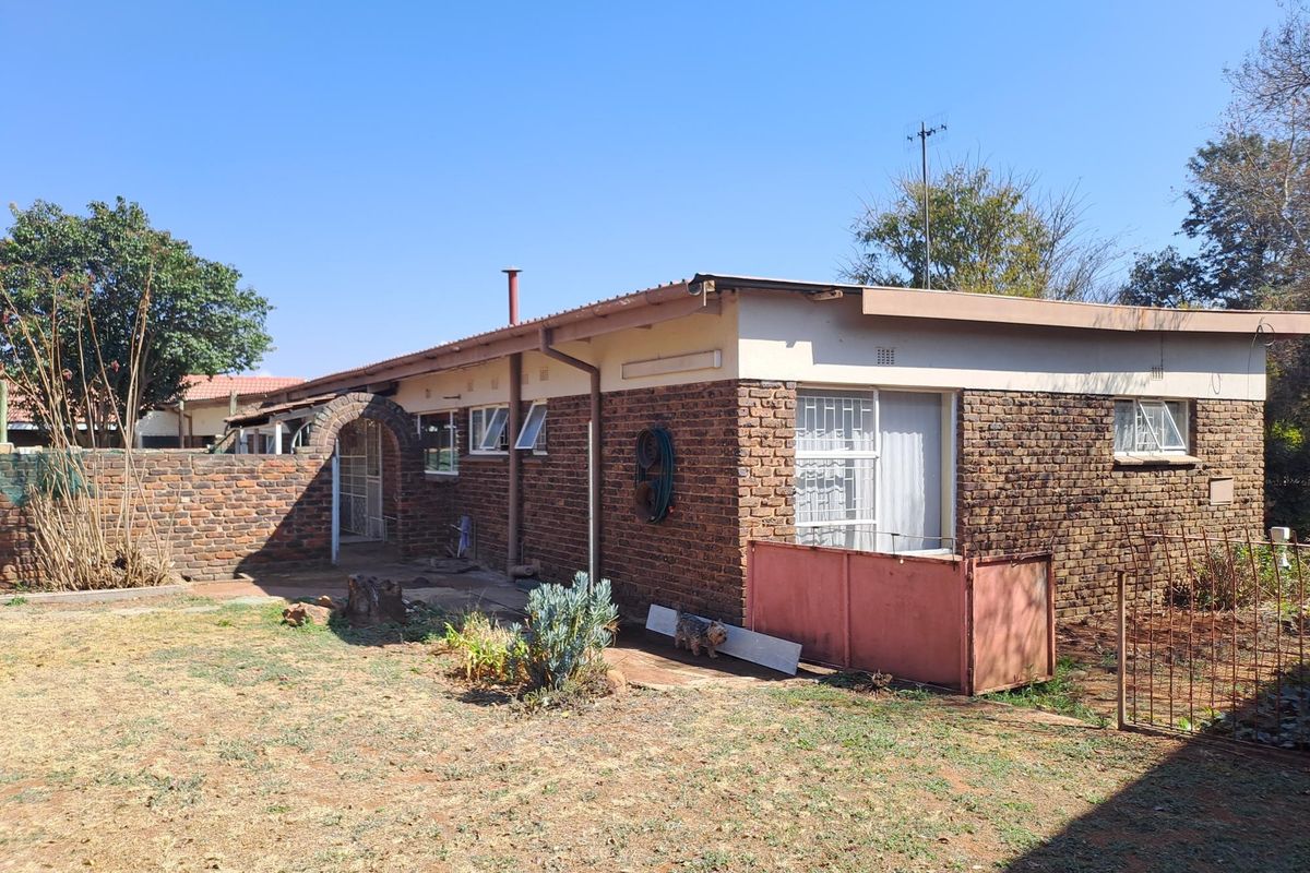 Rear view of a single-story face brick house featuring a metal roof, security bars on windows, and a brick boundary wall.