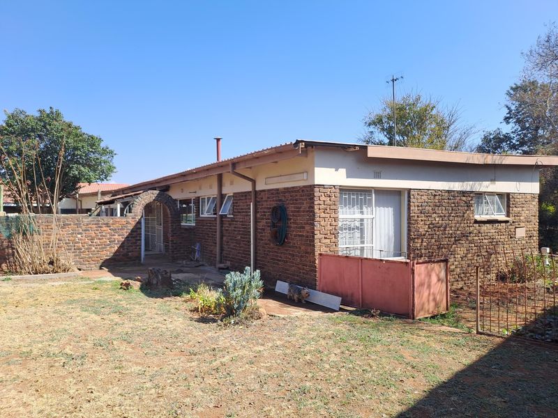 Rear view of a single-story face brick house featuring a metal roof, security bars on windows, and a brick boundary wall.