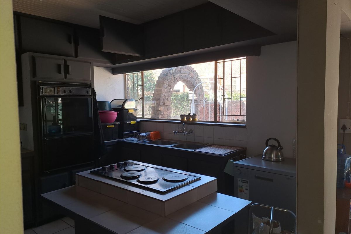 A functional kitchen featuring a central tiled island with an electric hob, built-in oven, and double basin sink with a view of the garden.