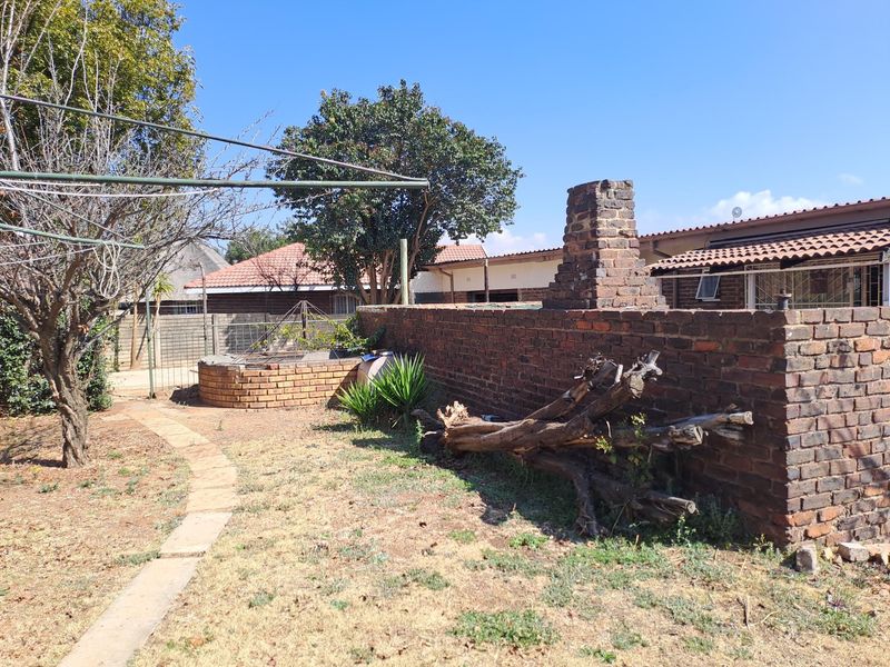 Rear garden area featuring a brick boundary wall with an integrated chimney, paved pathway, and established trees under a clear sky.