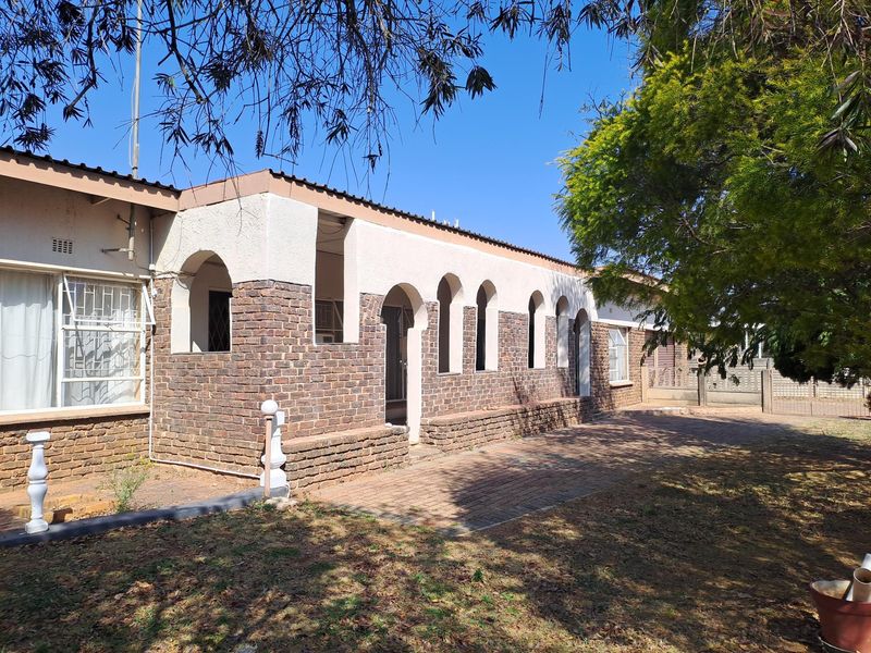 Rear exterior view of the house featuring a brick facade with arched architectural details and a paved patio area.