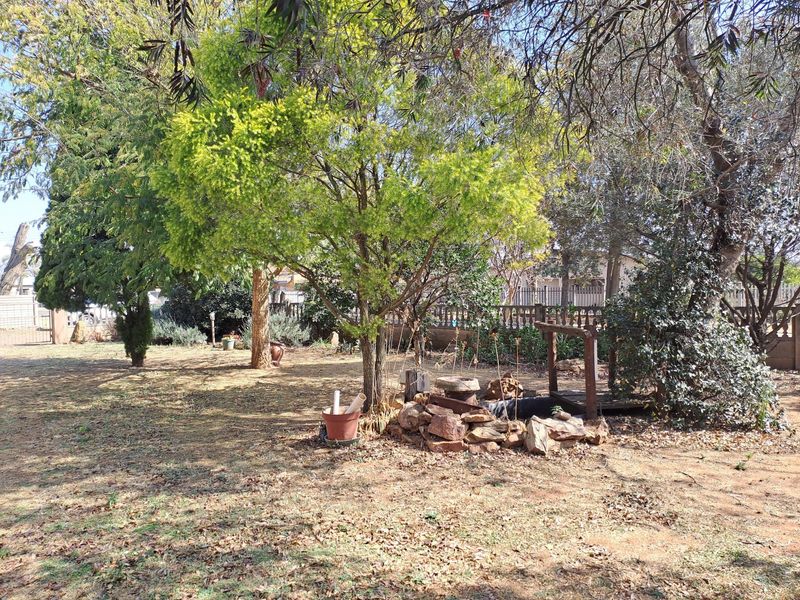 A spacious garden area featuring mature trees, stone landscaping elements, and perimeter fencing, offering a private outdoor space.