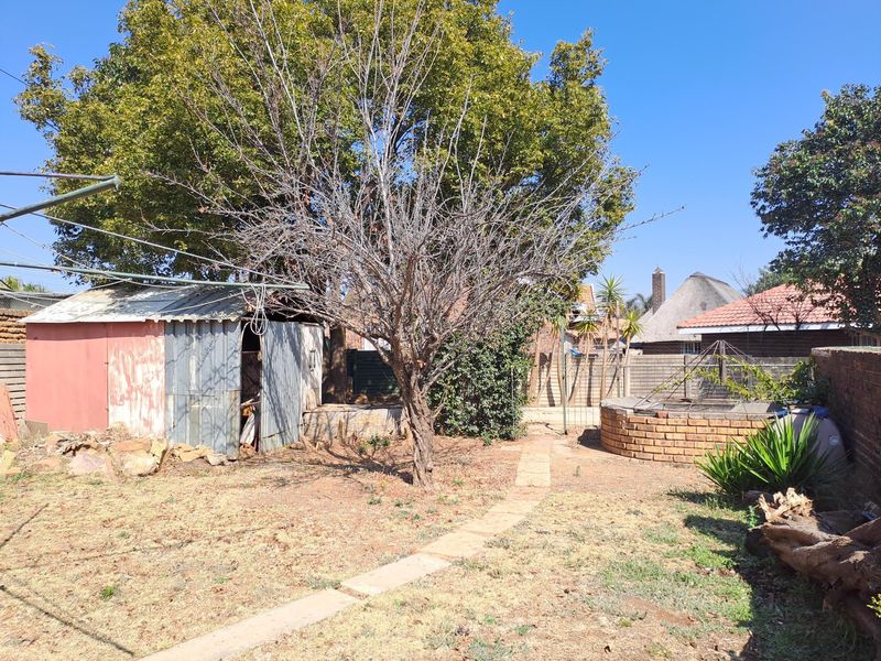 A rear garden area featuring a corrugated metal shed, a circular brick planter, and a paved pathway leading through the yard.