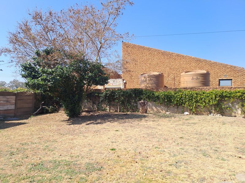 Rear garden area featuring a brick facade, two water storage tanks, and a precast concrete boundary wall with established climbing plants.