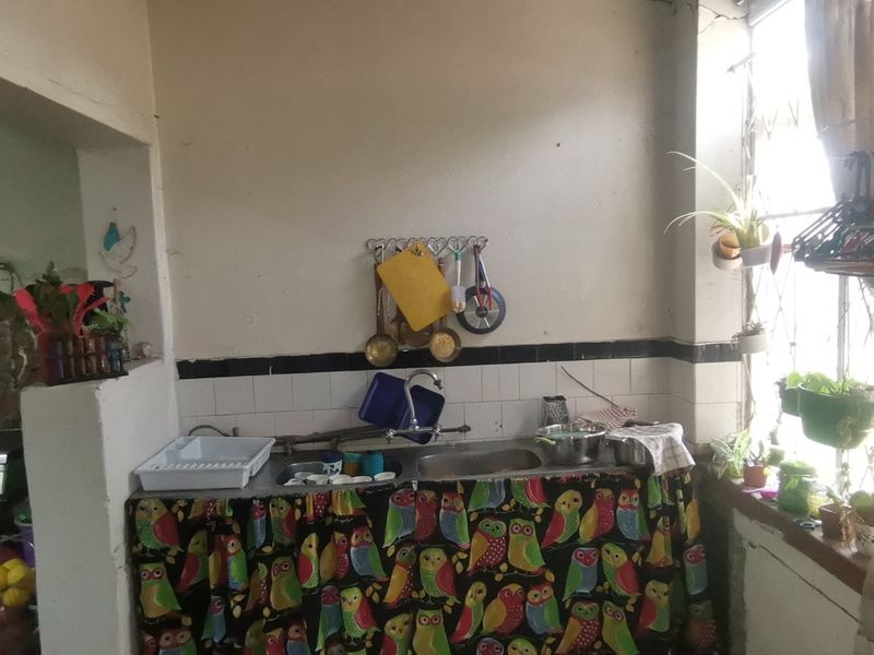 A dated kitchen area featuring a stainless steel sink, tiled splashback, and a freestanding stove, requiring significant cosmetic updates and wall repairs.