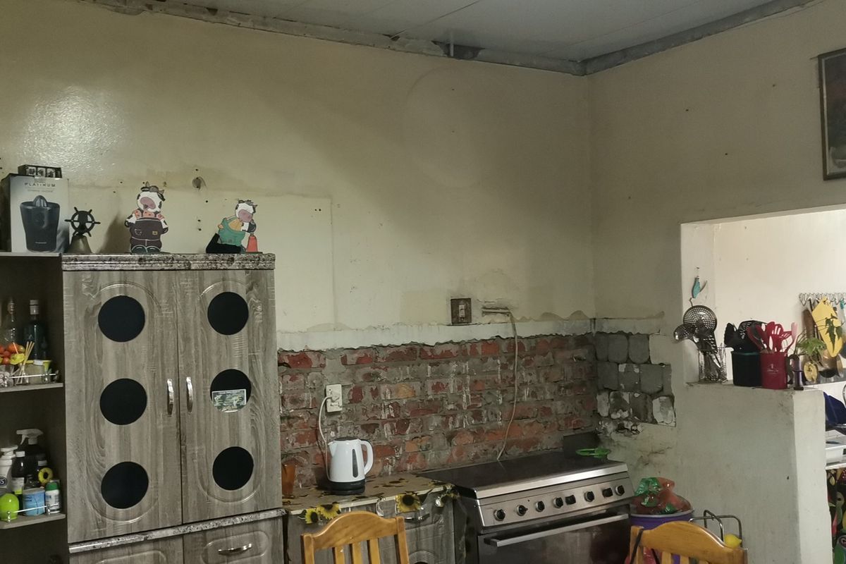 A kitchen area featuring an exposed brick wall, freestanding stove, and double sink, currently requiring significant renovation and finishing of wall surfaces.